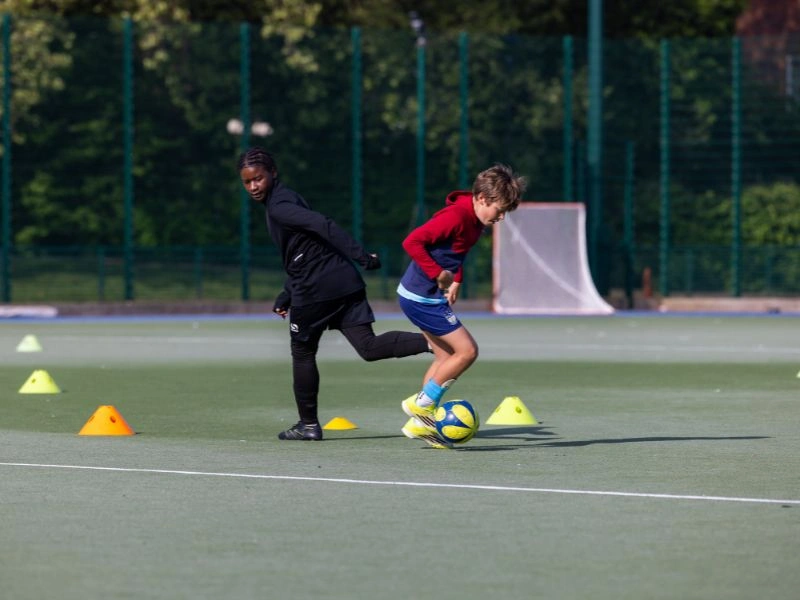 EFA player dribbling during a one-week football trial in London, with coach observing in the background